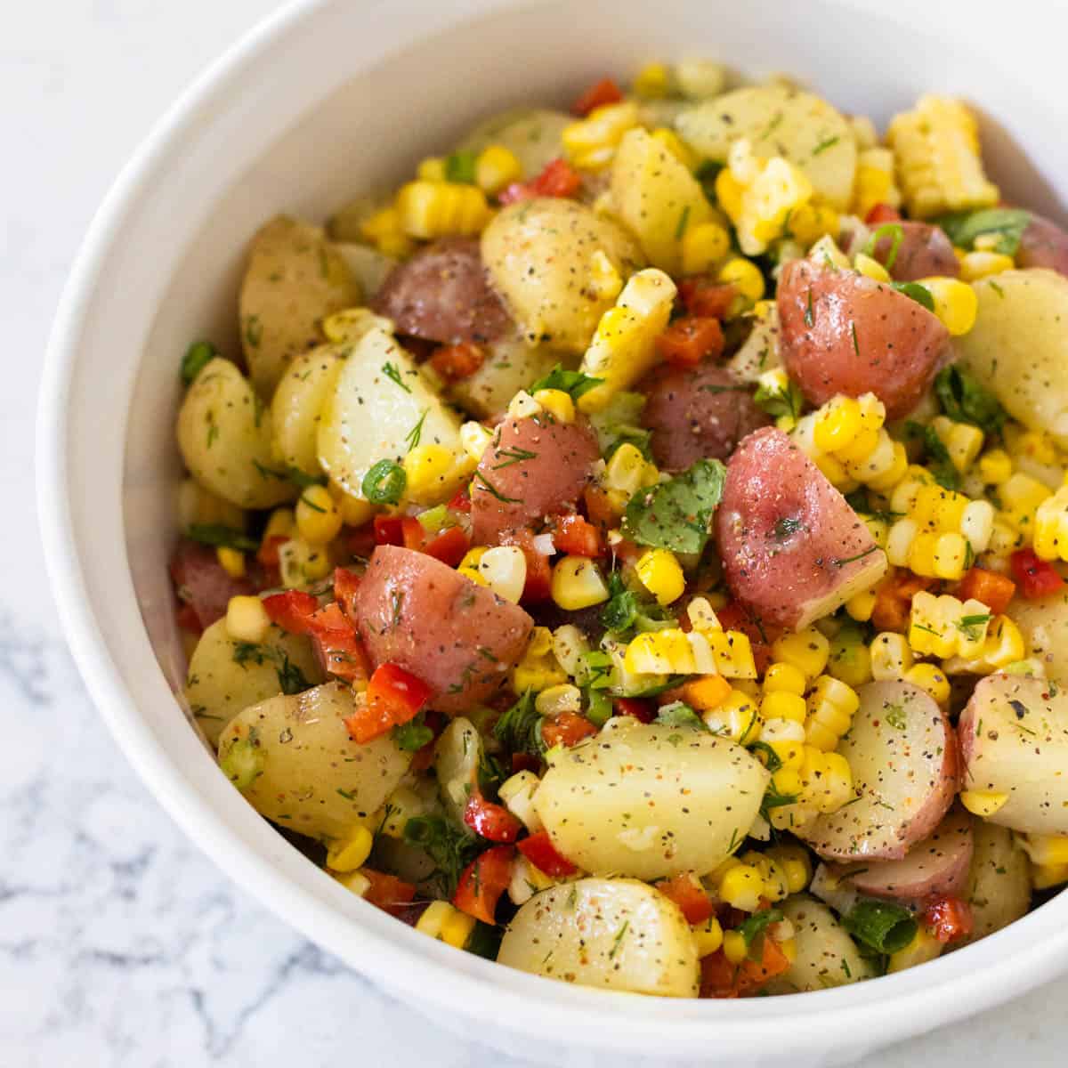 A white dish filled with potato salad mixed with corn and red bell peppers.