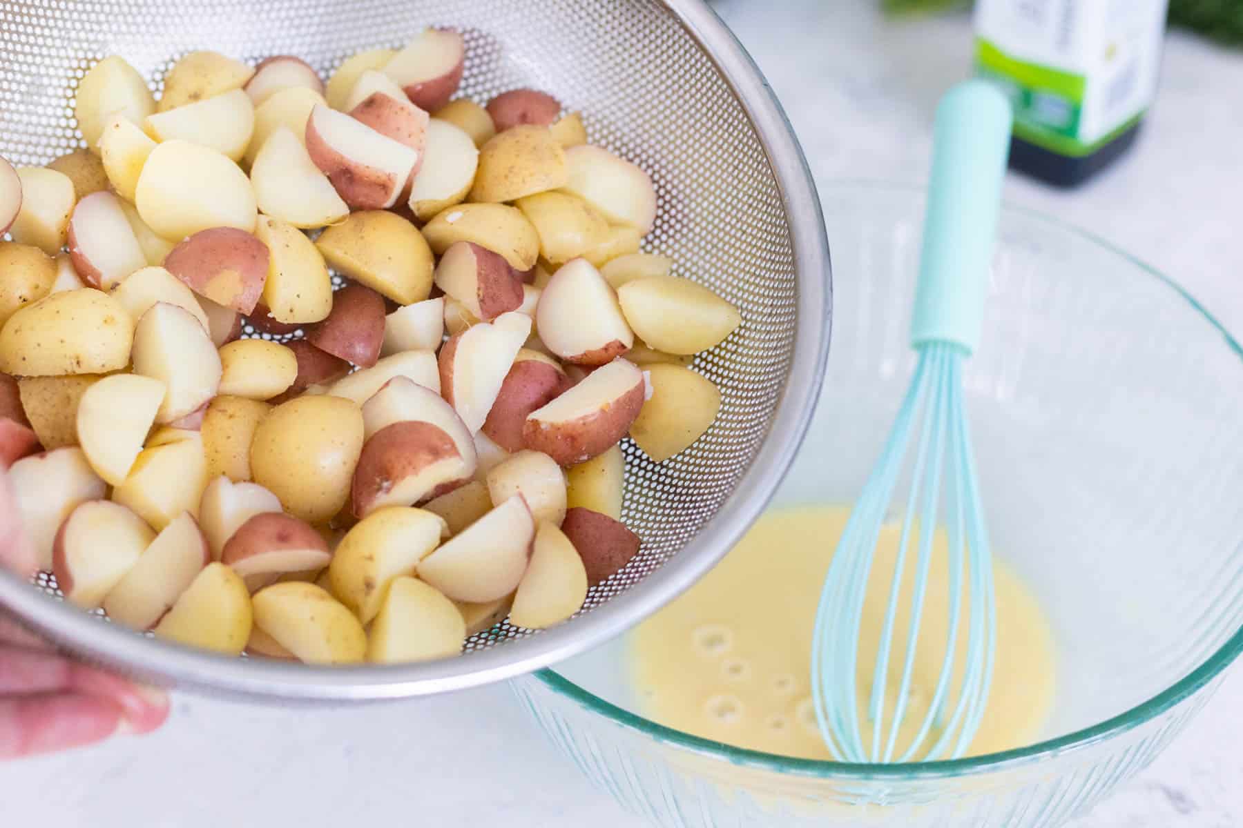 The potatoes are being poured into the mixing bowl with the mustard vinaigrette.