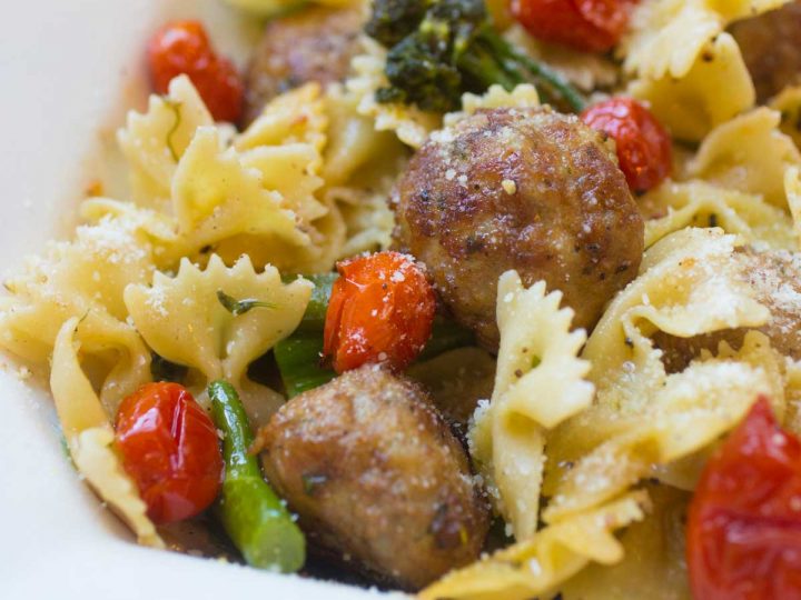 Bow tie pasta is tossed with roasted broccolini, roasted tomatoes, and chicken meatballs.