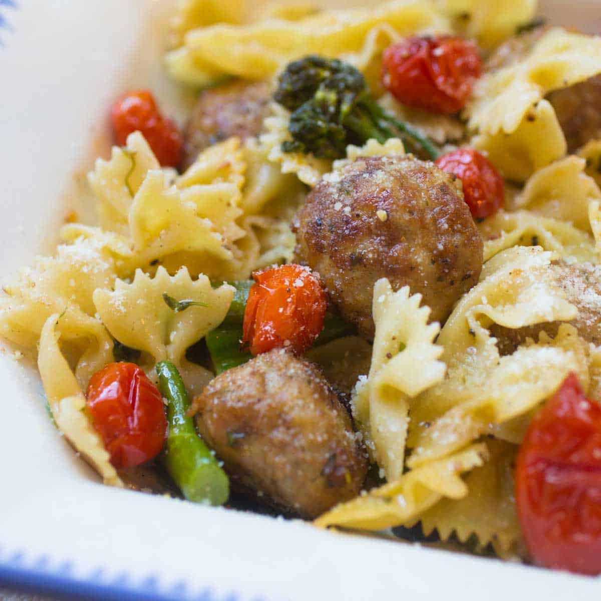 Bow tie pasta is tossed with roasted broccolini, roasted tomatoes, and chicken meatballs.