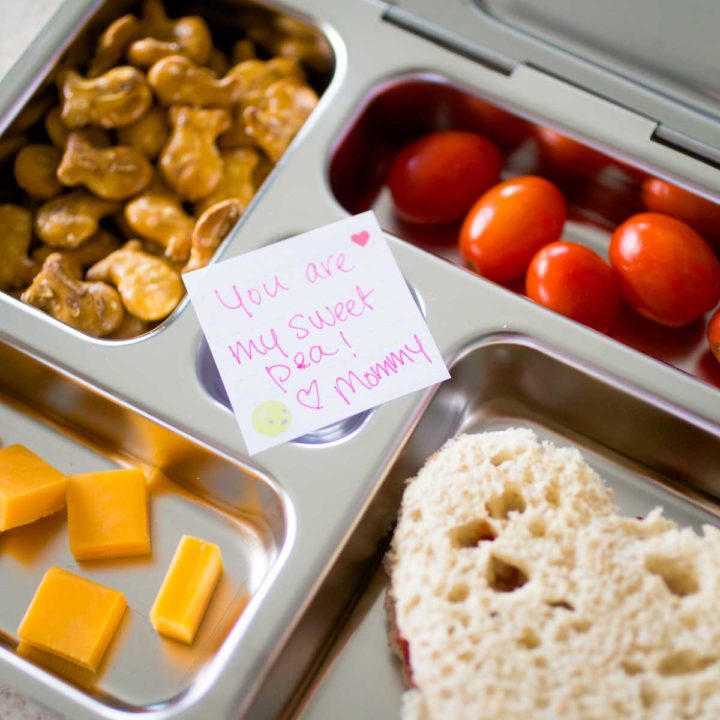 A bento lunchbox has finger foods and a love note from mom for a Kindergartener.