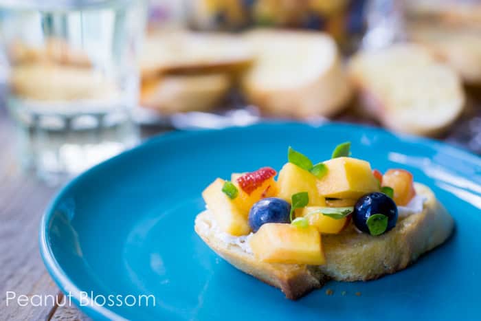 A slice of crostini toast topped with the peach blueberry salsa on a blue plate.