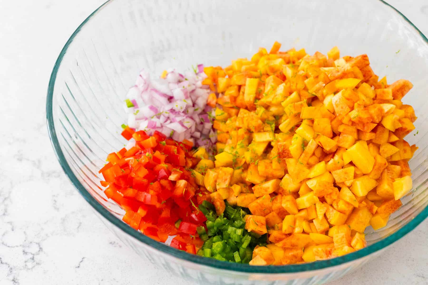 The mixing bowl is filled with diced peaches, diced red peppers, diced red onion, and minced jalapeno.