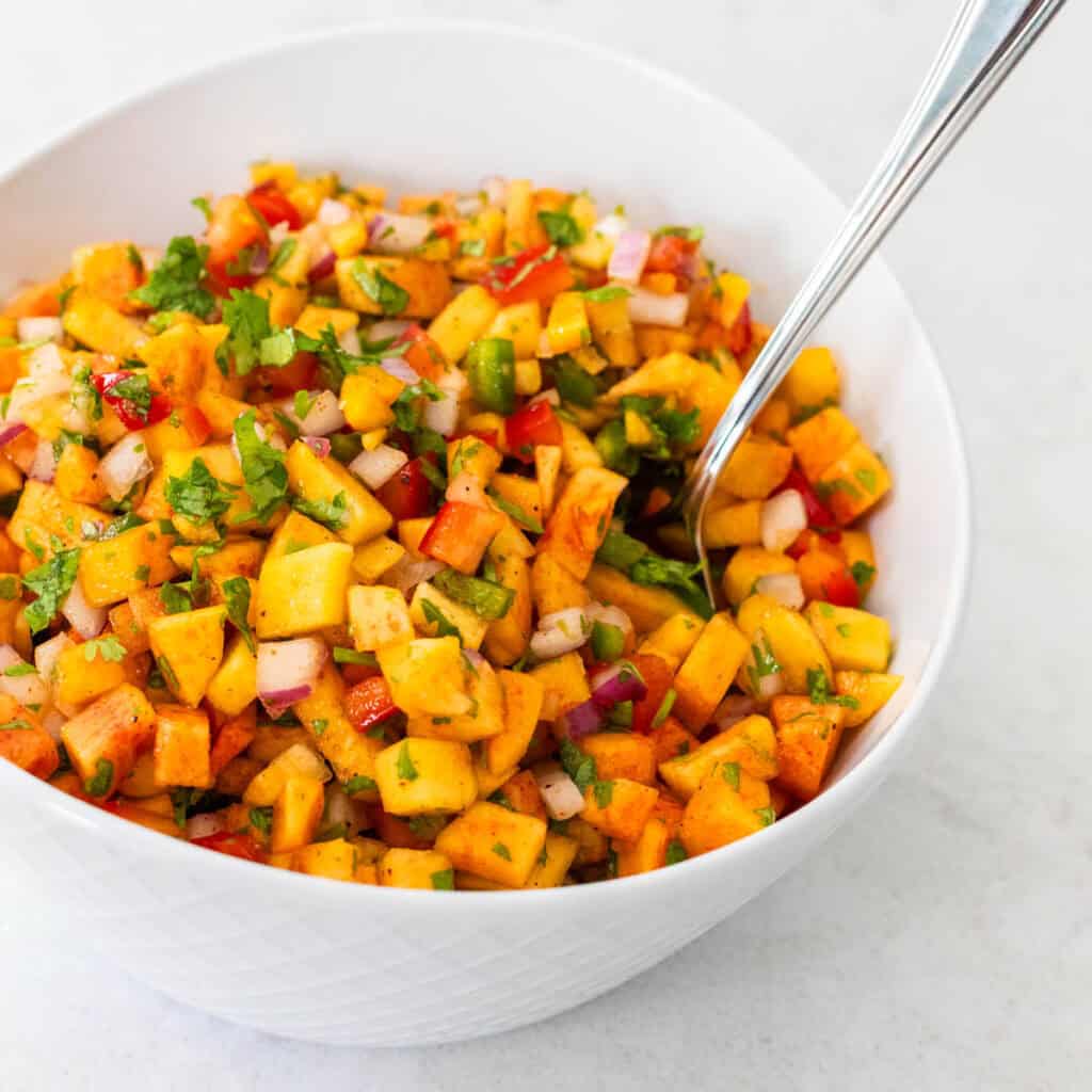 A fresh peach salsa made with diced peaches, red pepper, and jalapeno is served in a white bowl.