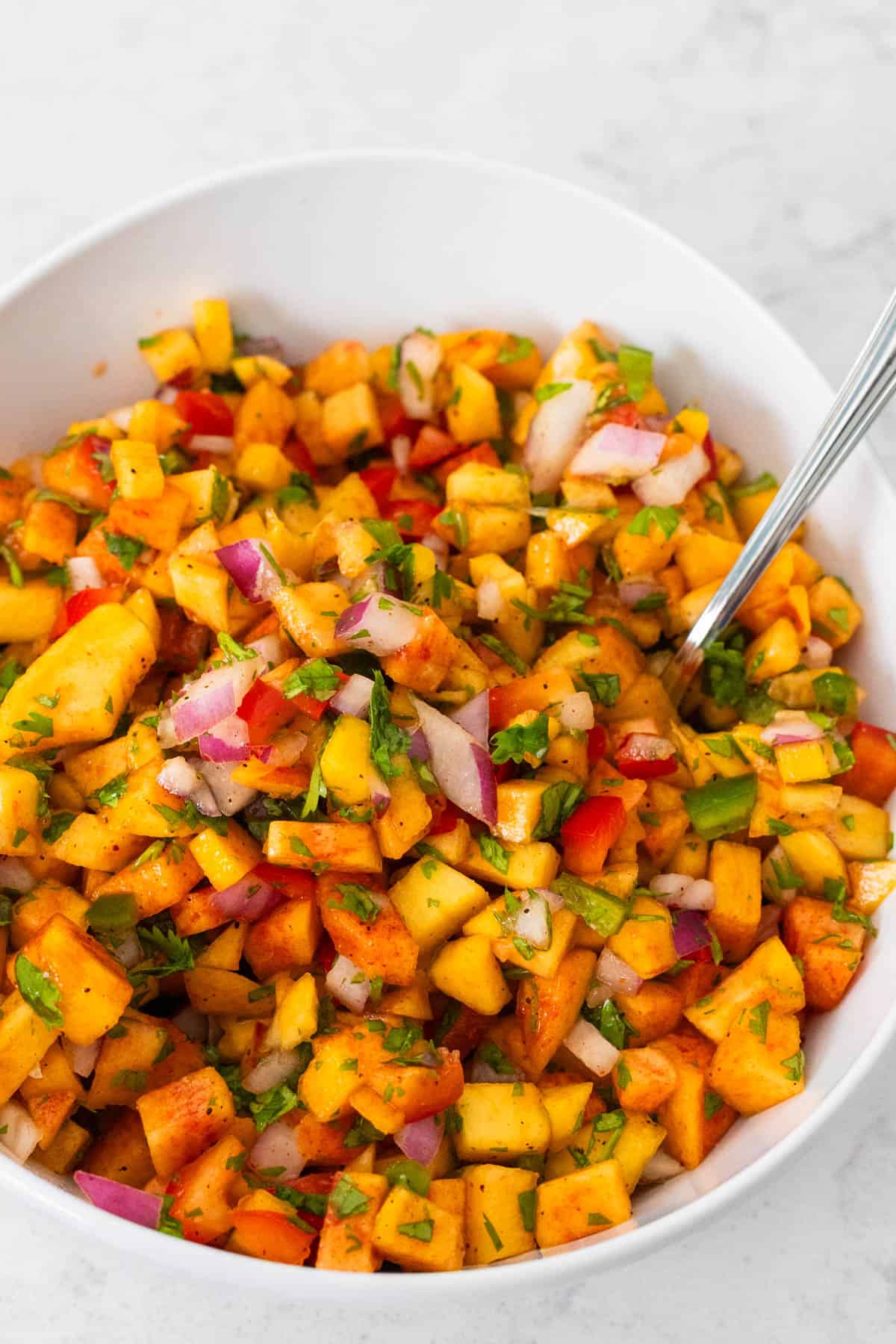 The finished peach salsa is in a white serving bowl with a spoon.