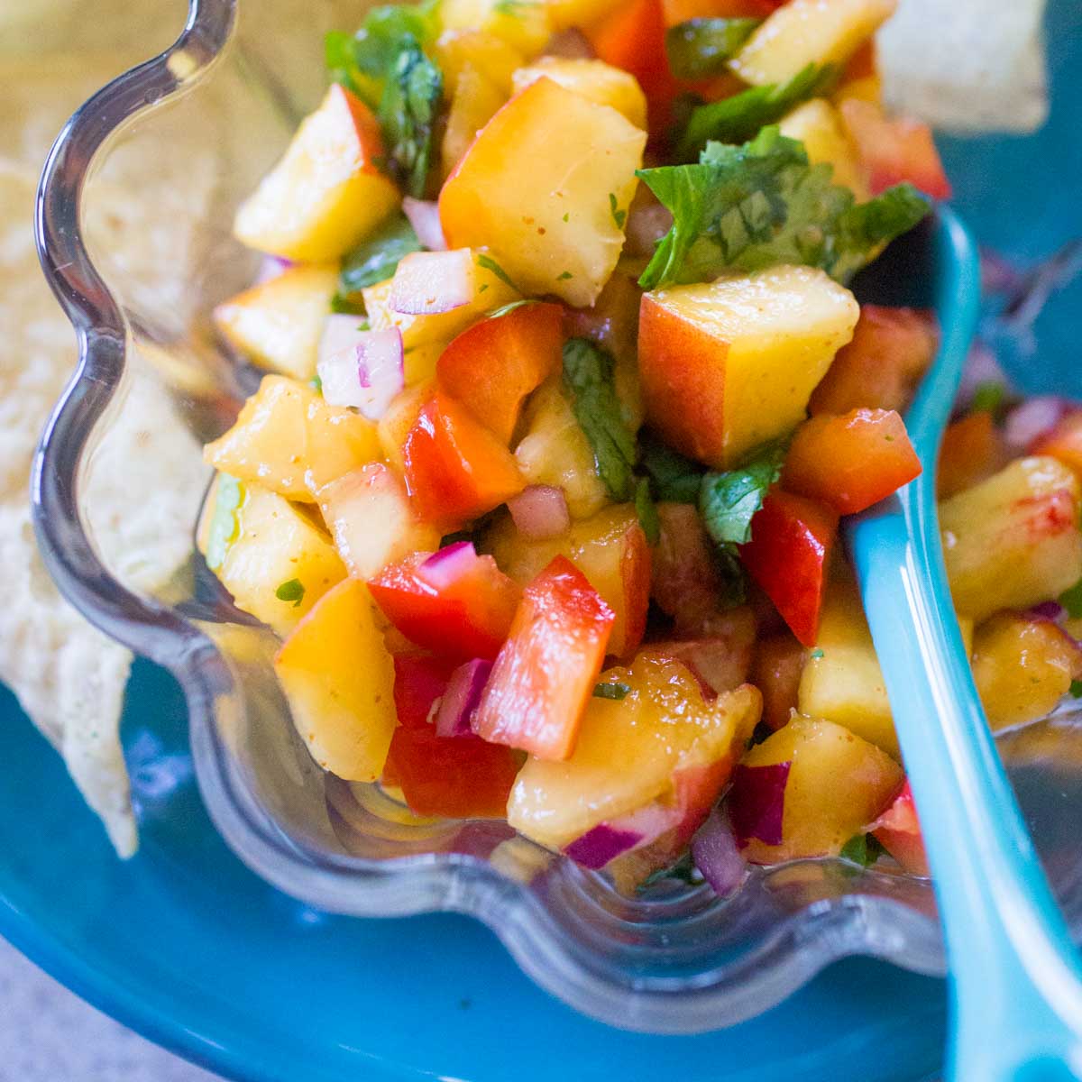 A bowl of homemade chunky peach salsa has a blue spoon for serving.