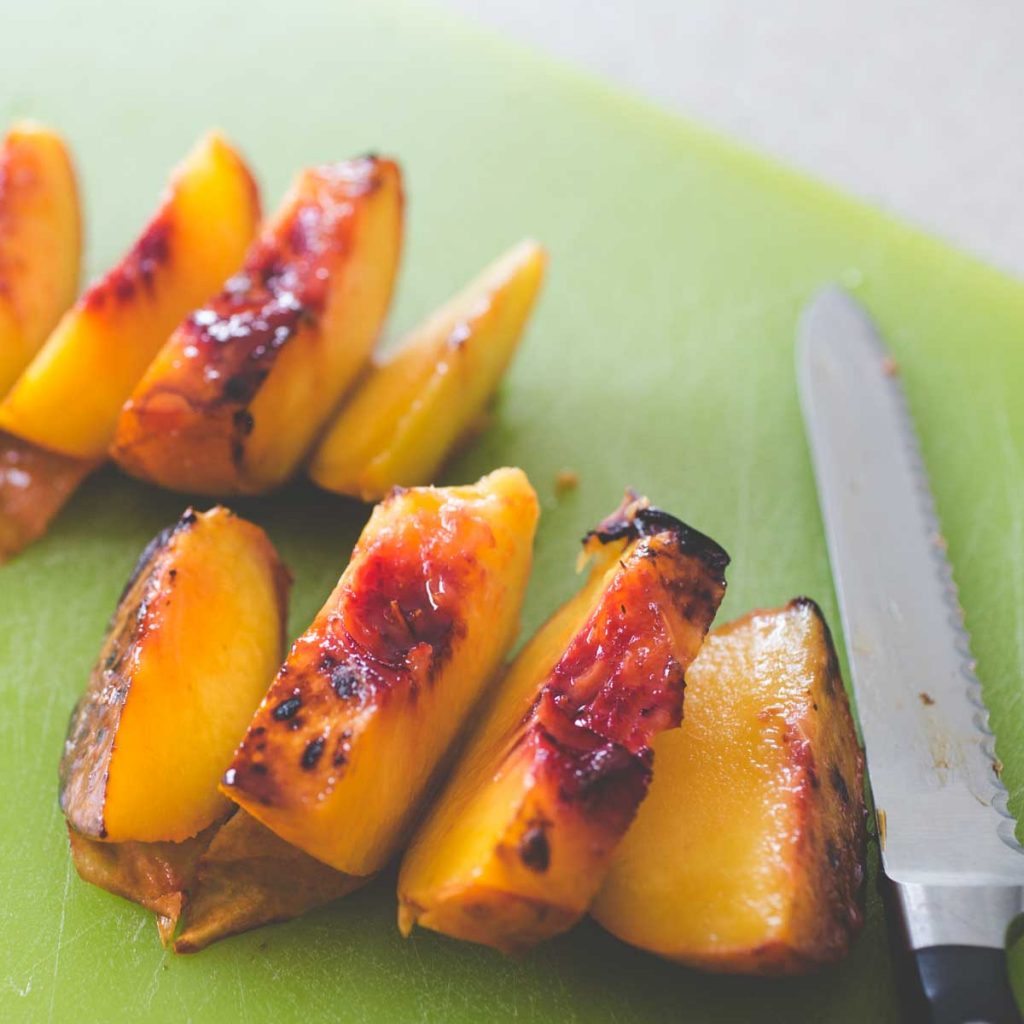 Sliced grilled peaches are lined up on a cutting board.
