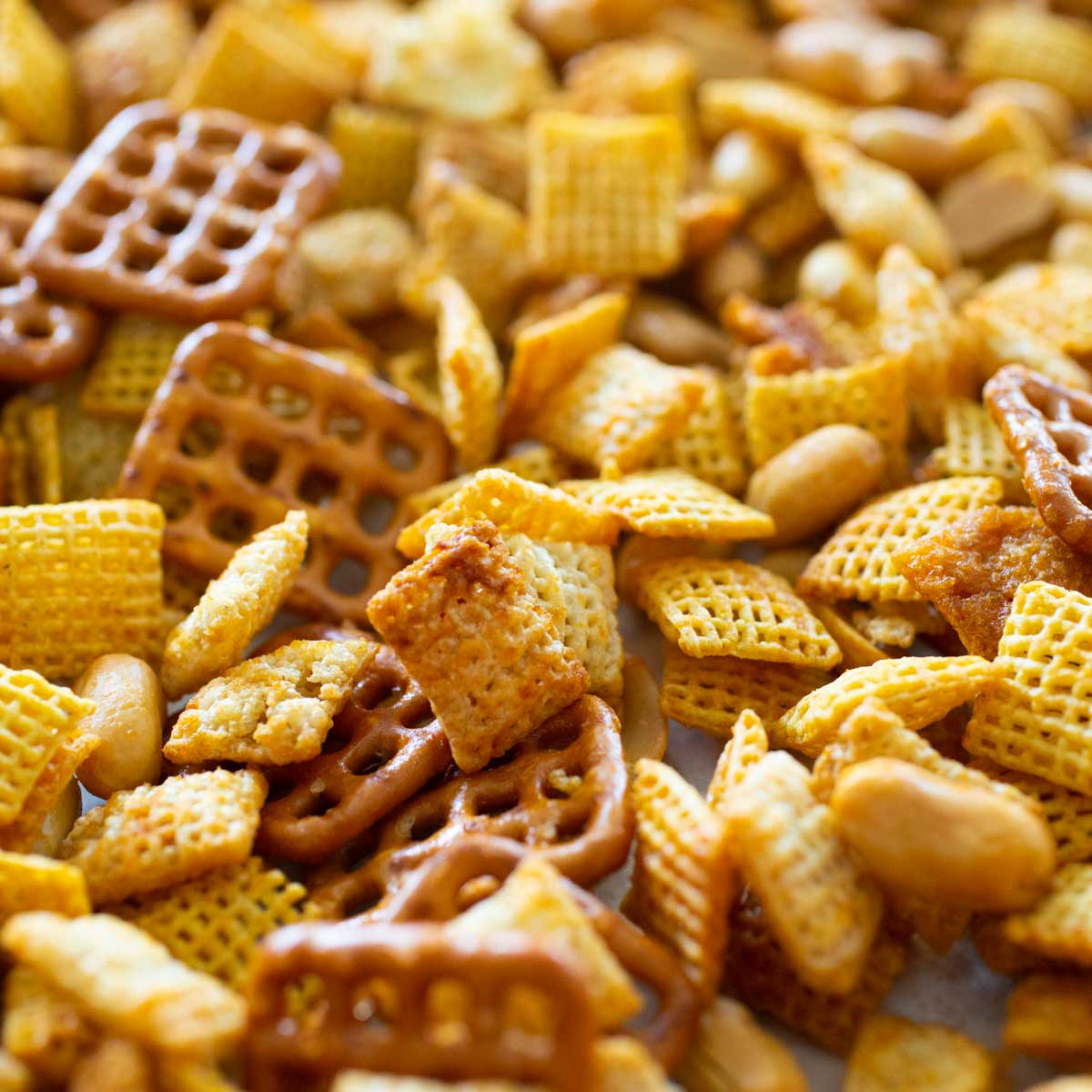 Sweet and spicy honey sriracha chex mix has square pretzles, cereal, and peanuts mixed together.