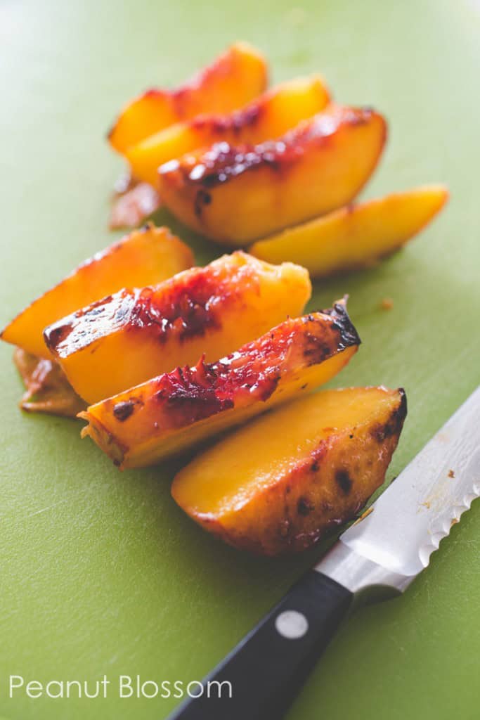 The broiled peaches have been sliced into wedges on a cutting board. The serrated knife is off to the side.