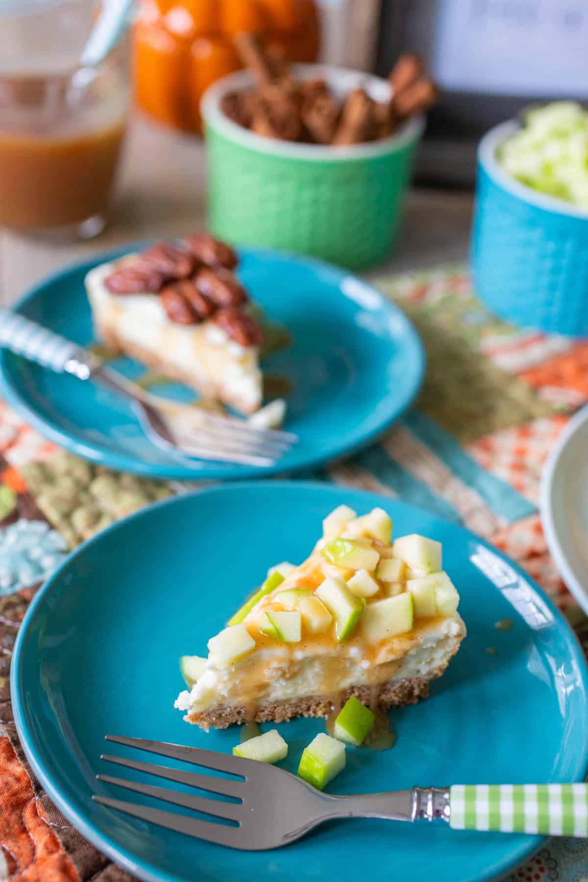 The slice of caramel apple and pecan pie cheesecakes are served on blue plates.
