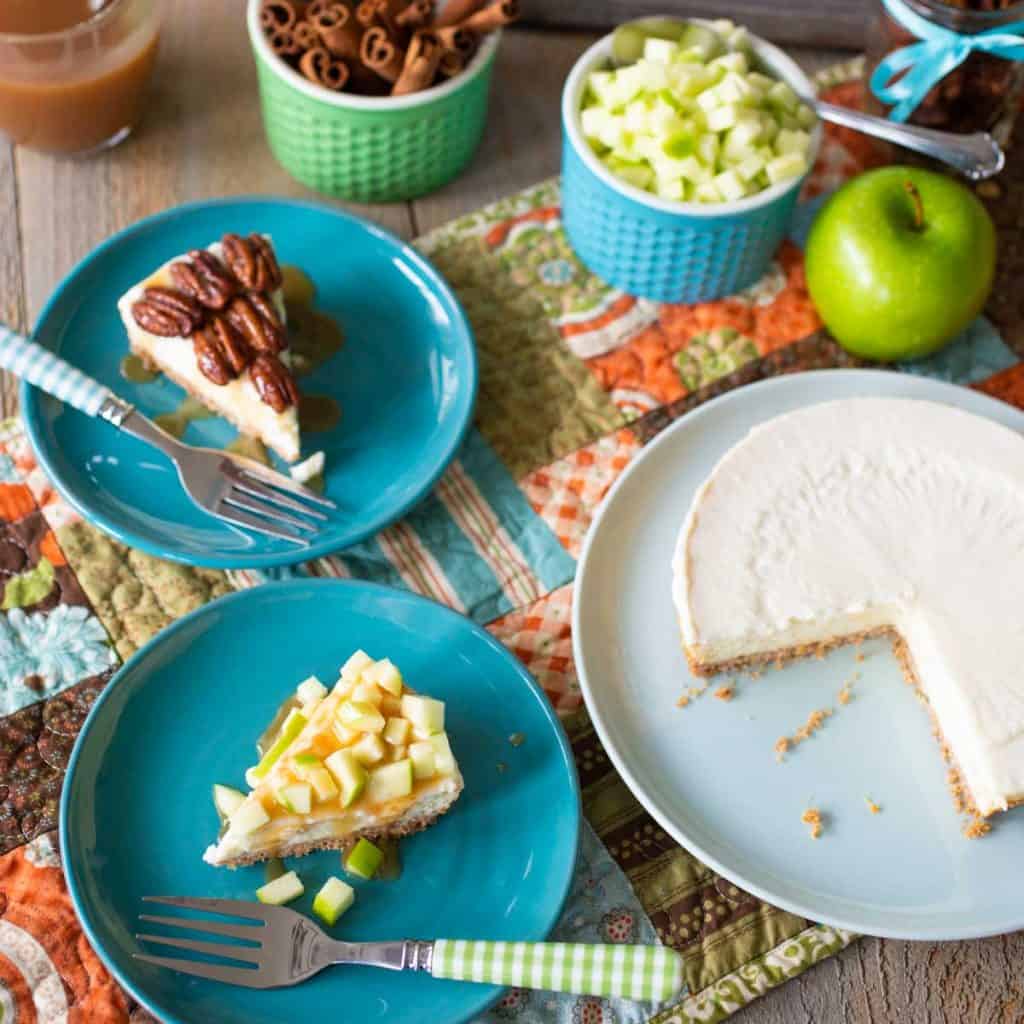 A plain cheesecake has been cut into two slices: One has pecans and caramel, the other has fresh apples and caramel.