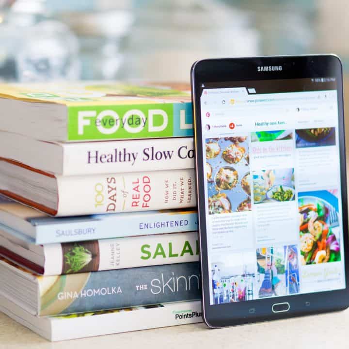 A stack of cookbooks is next to a digital tablet.