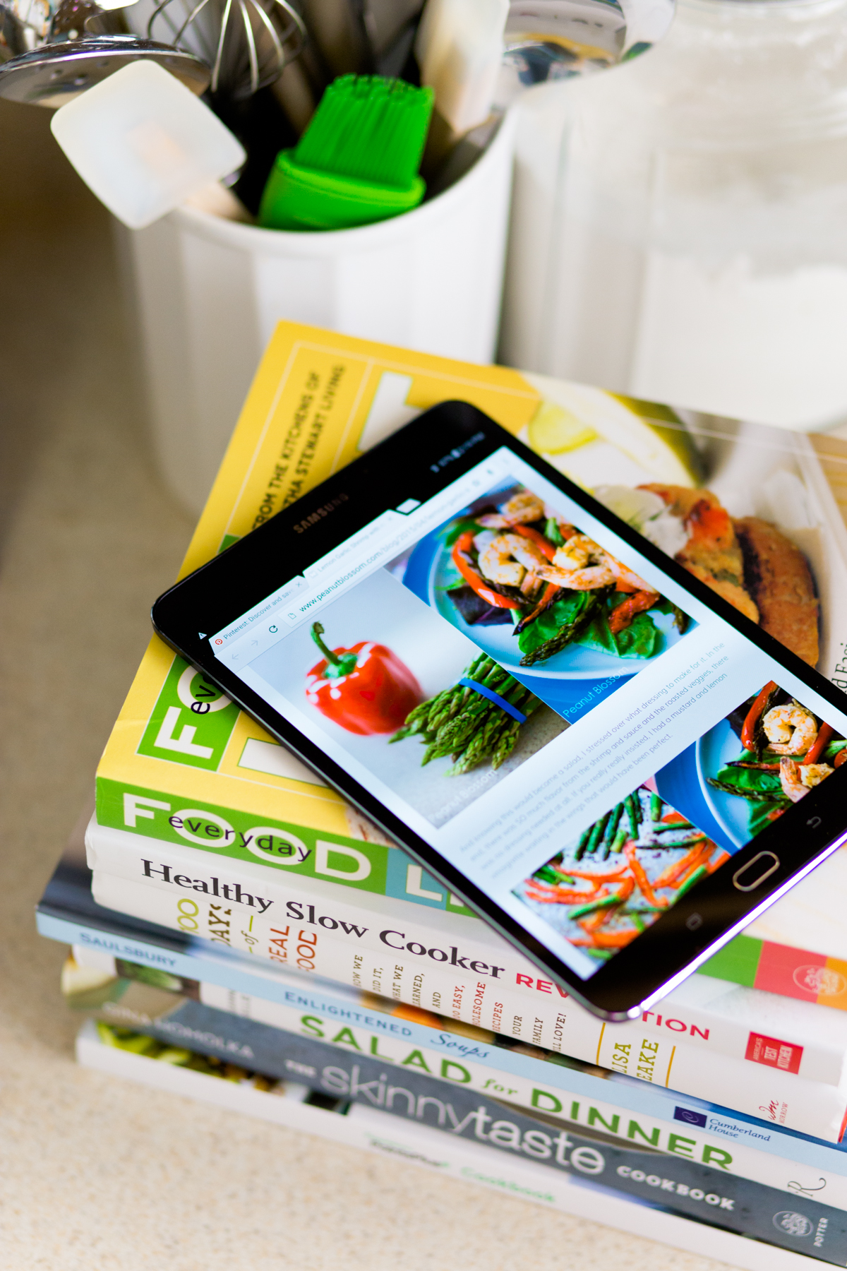 a stack of healthy cookbooks has a digital tablet sitting on top of the pile.