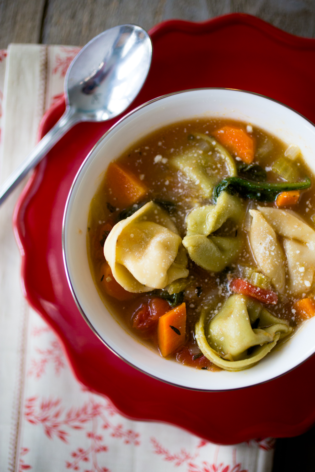 Weight Watchers friendly tortellini soup in a bowl with a spoon on a red plate.