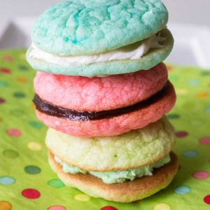 A trio of macaron-inspired cake sandwich cookies in green, pink, and blue colors on a polka dot napkin.