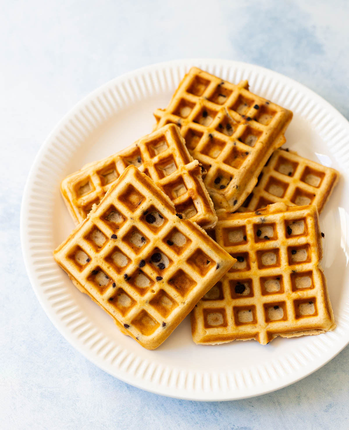 A stack of waffles are on a white plate.