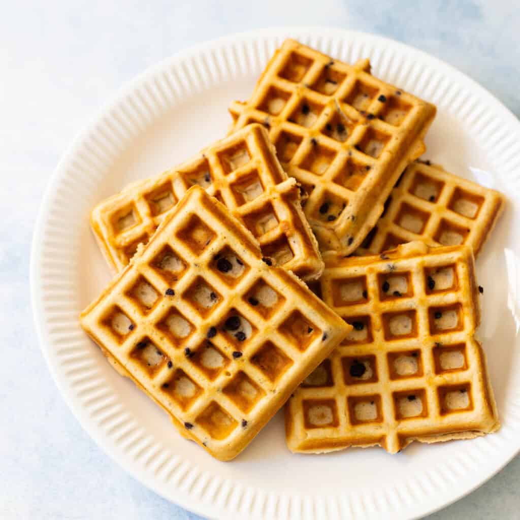 A white plate is piled up with deliciously crispy waffles.