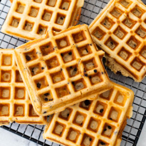 Fresh griddled peanut butter waffles with mini chocolate chips are cooling on a rack.