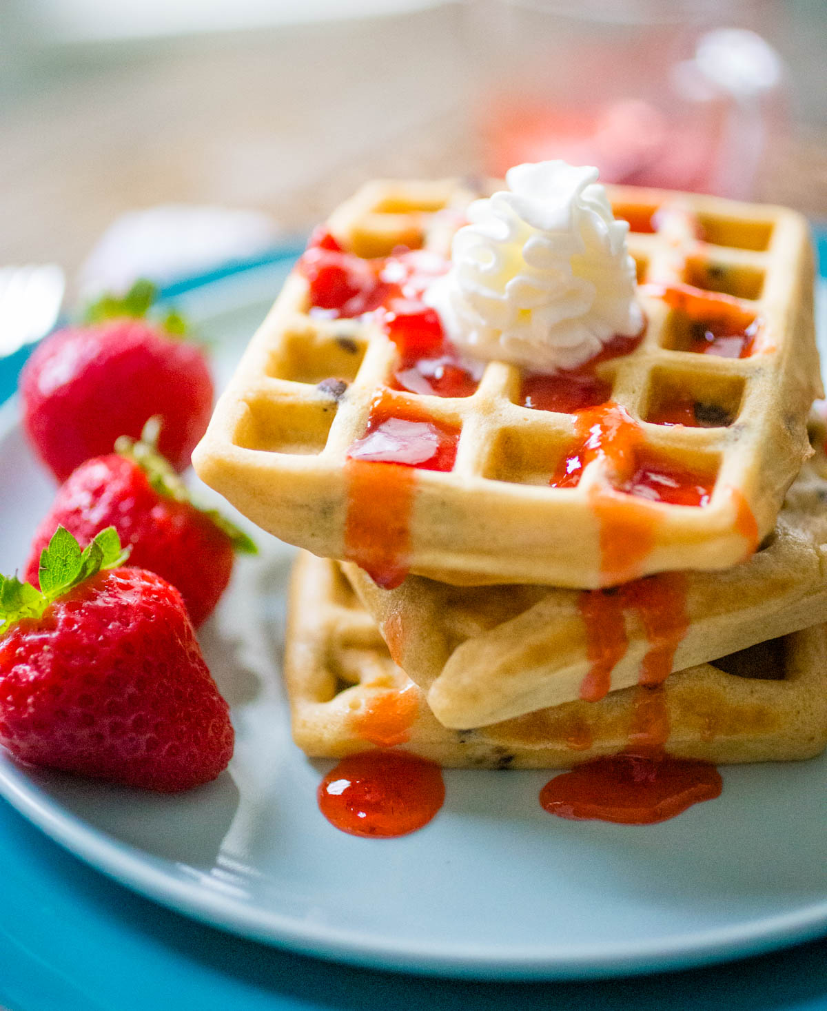 The stack of peanut butter waffles has strawberry jelly running down the sides and a dollop of whipped cream on top.