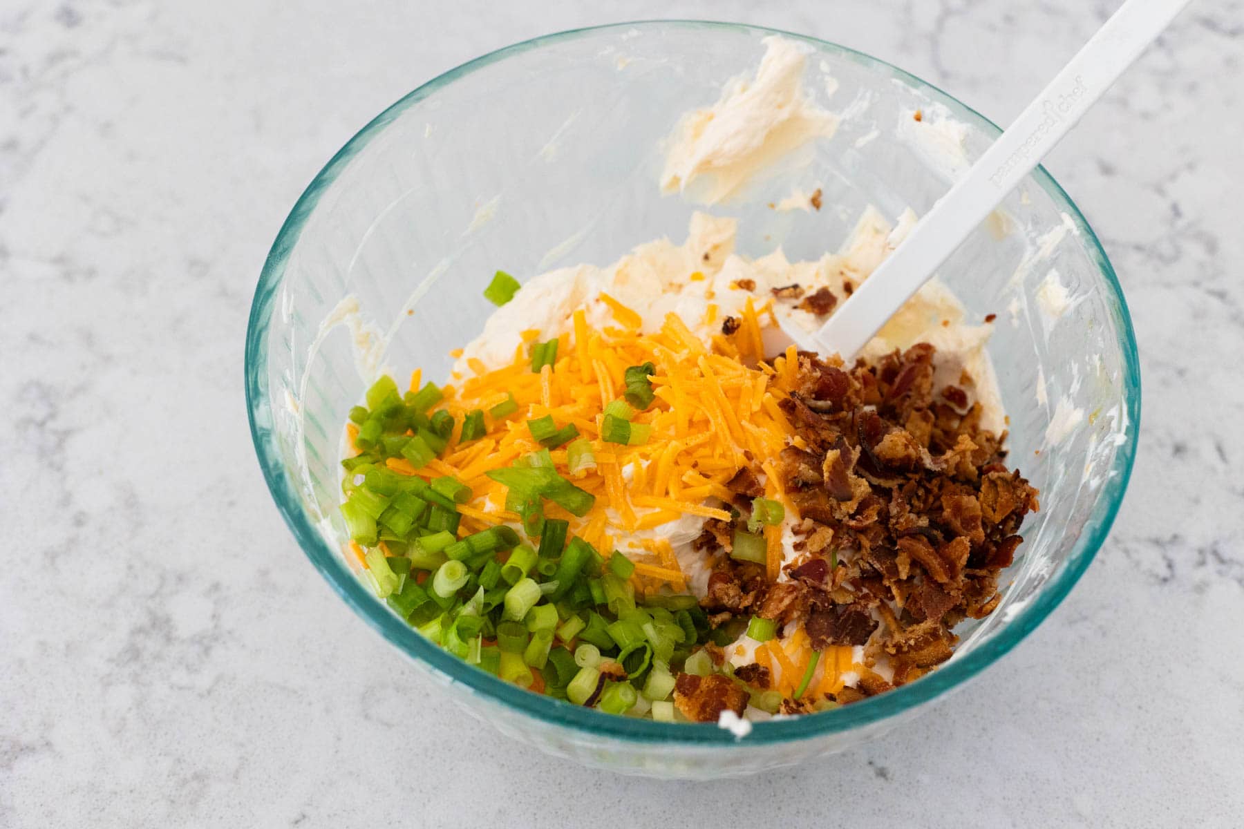 The mixing bowl has bacon, shredded cheese, and green onions on top.