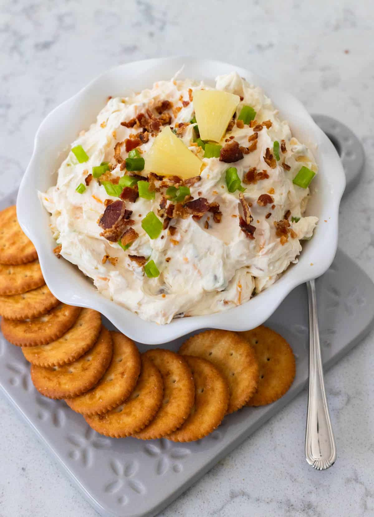 The finished dip has crumbled bacon and pineapple on top and is served with a platter of crackers.