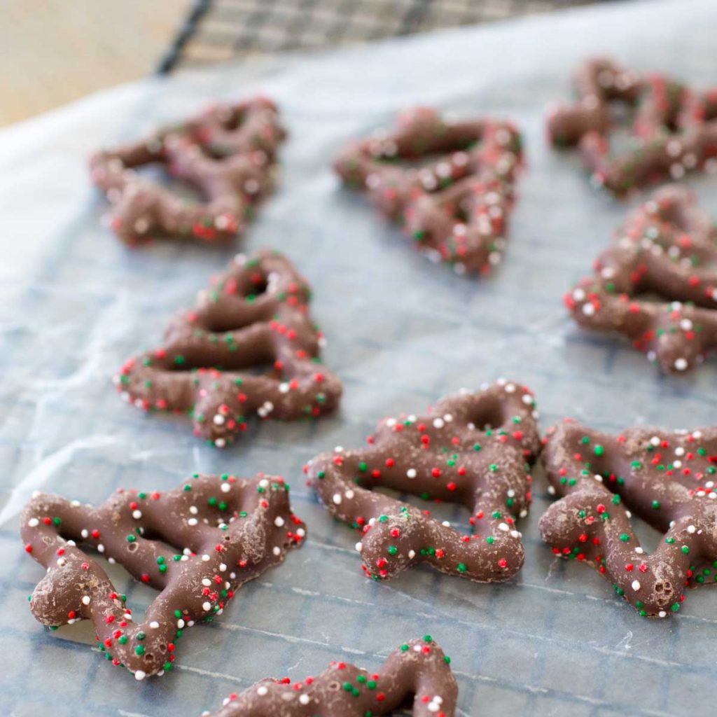 Wax paper has drying tree-shaped pretzels covered in melted chocolate and red, green, and white sprinkles.