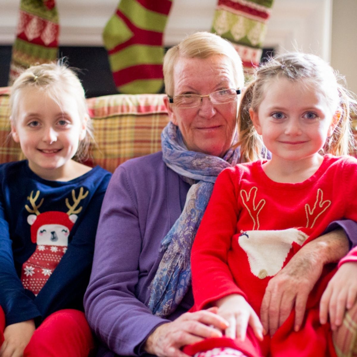 A Grandma sits on a couch dressed for Christmas with her two granddaughters.