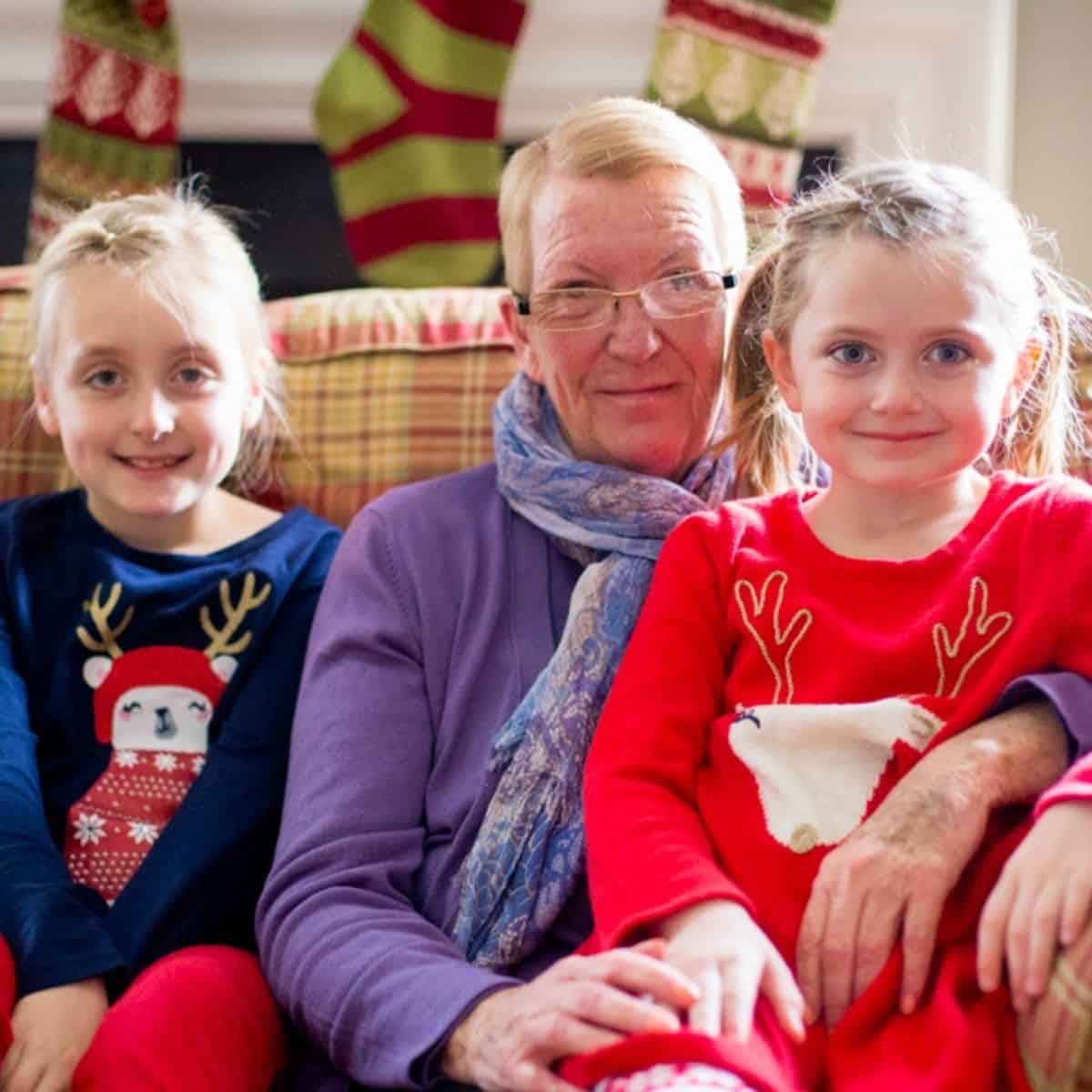 A Grandma sits on a couch dressed for Christmas with her two granddaughters.