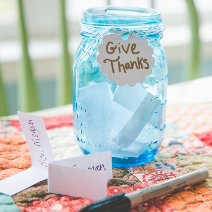 A blue gratitude jar sits on a table next to slips of paper and a Sharpie.