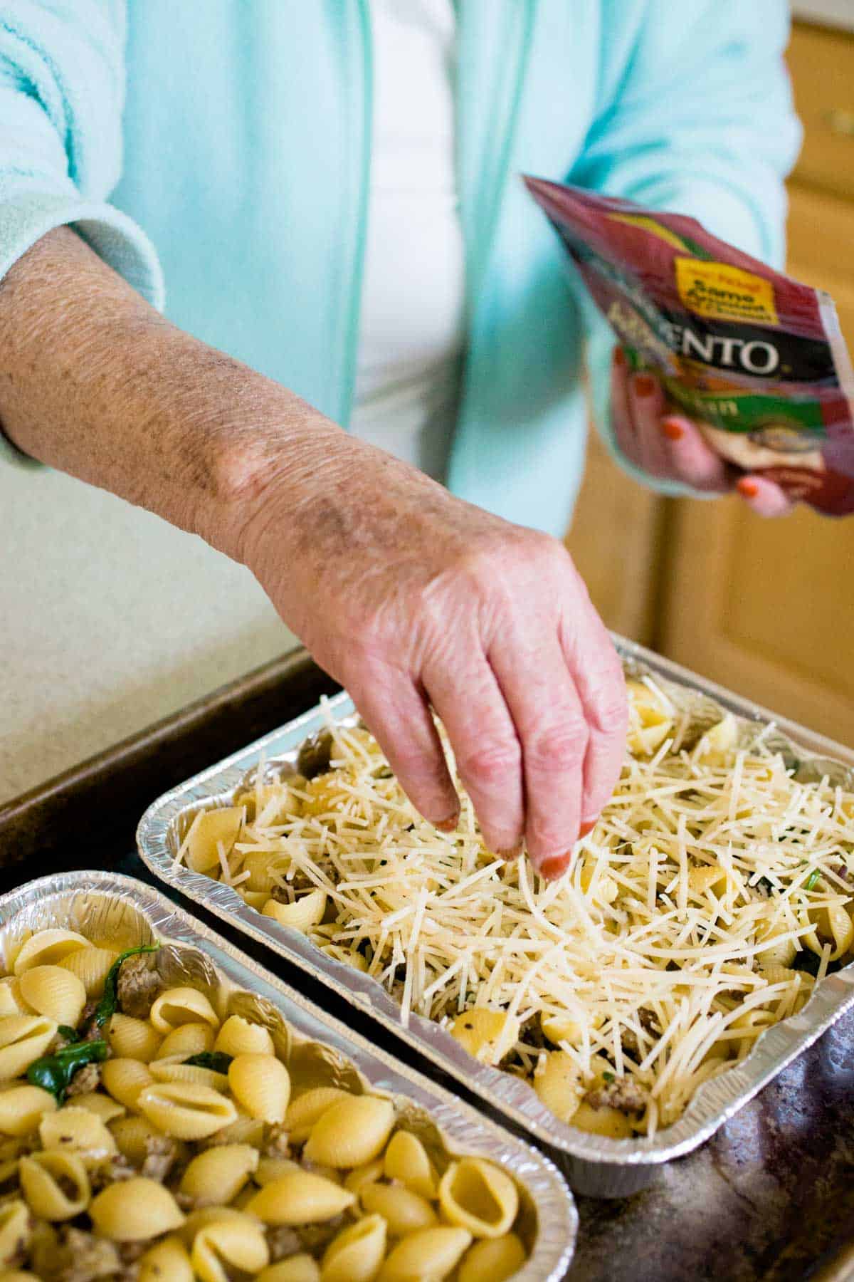 My mom is sprinkling cheese over the filled baking pans.