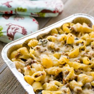 A pan of baked Italian sausage pasta casserole has a pair of oven mitts in the background.