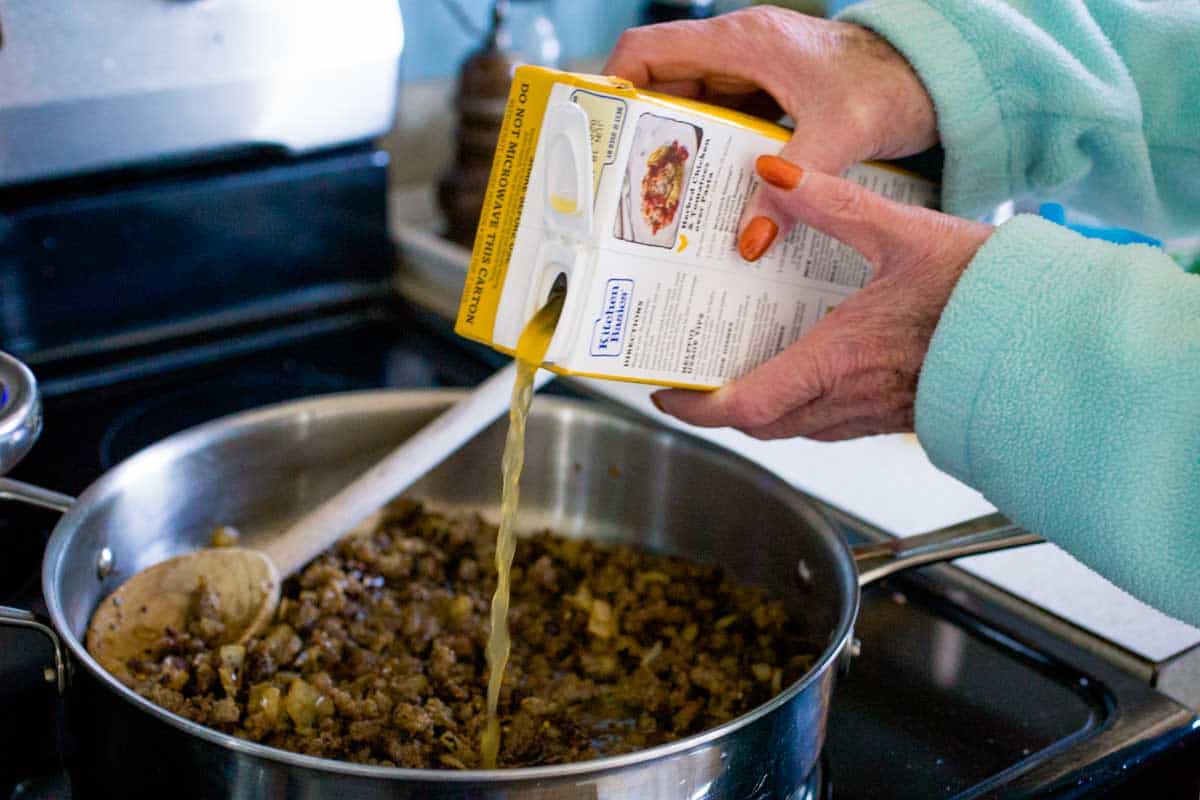 My mom's hands are pouring in the chicken broth for her recipe.