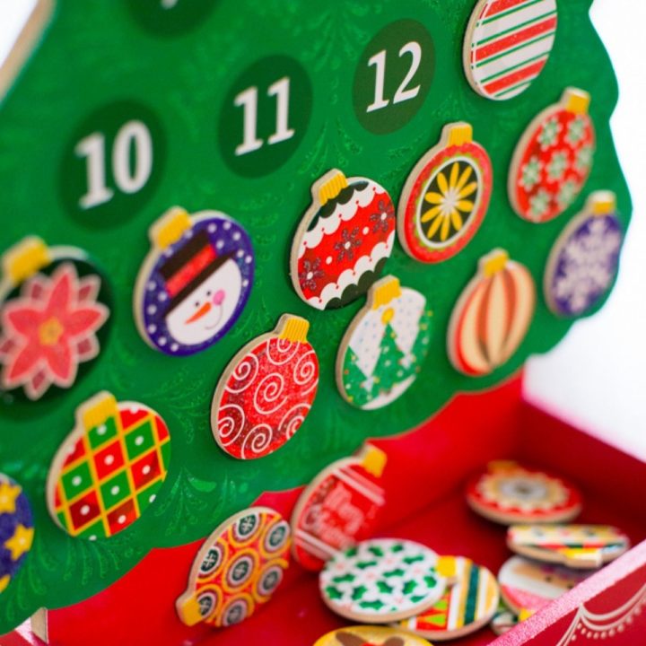 A wooden Advent calendar has colorful painted ornaments hanging on a wooden tree.