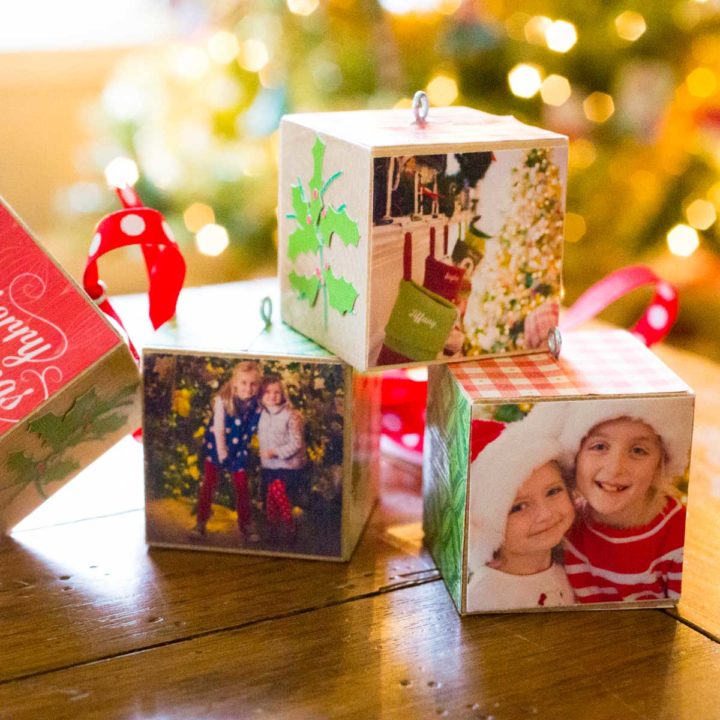 A stack of wooden photo ornaments sits in front of a Christmas tree.