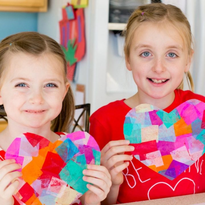 Two girls hold up their heart-shaped paper crafts.