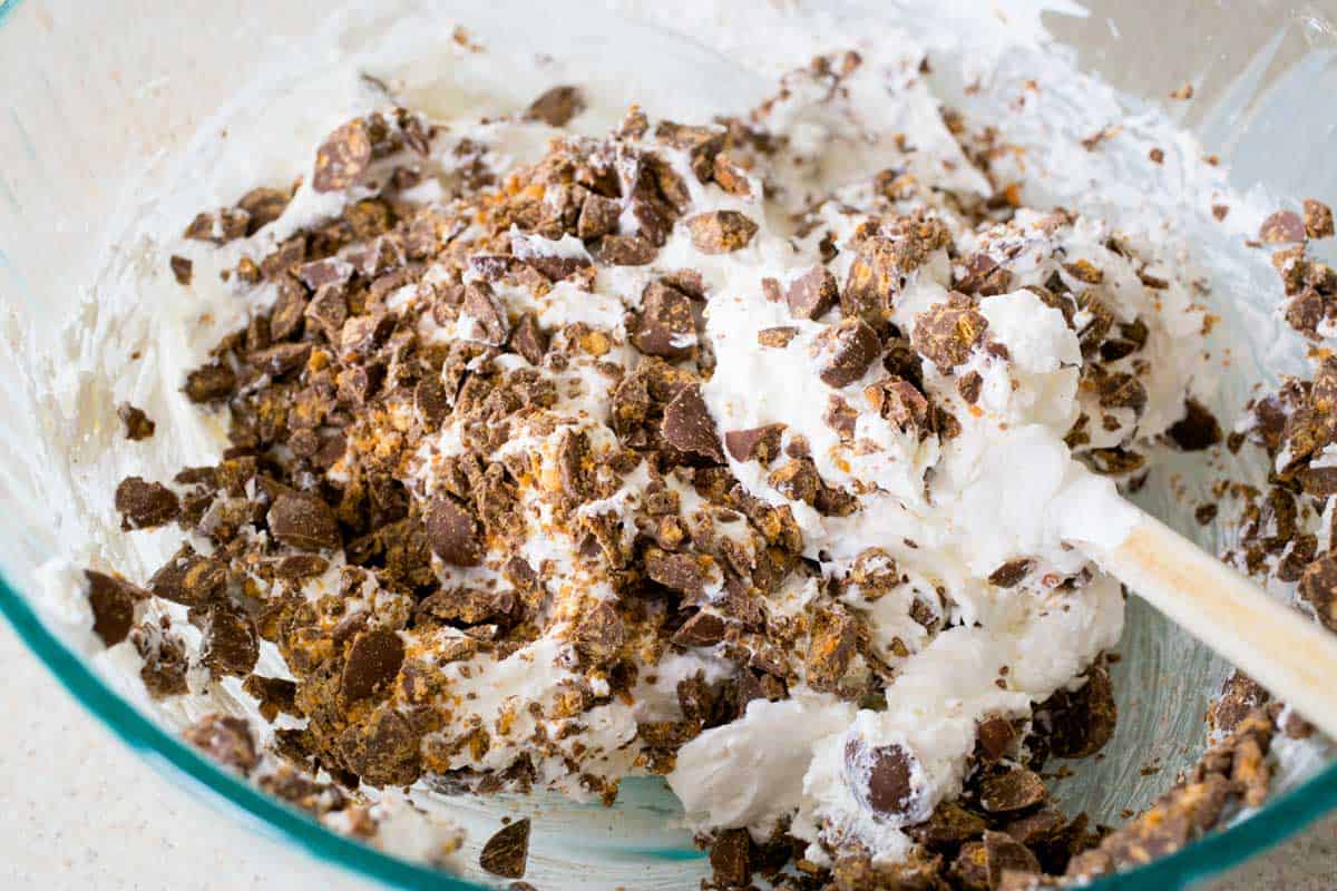 The creamy pie filling has the chopped chocolate being folded in by a spatula.