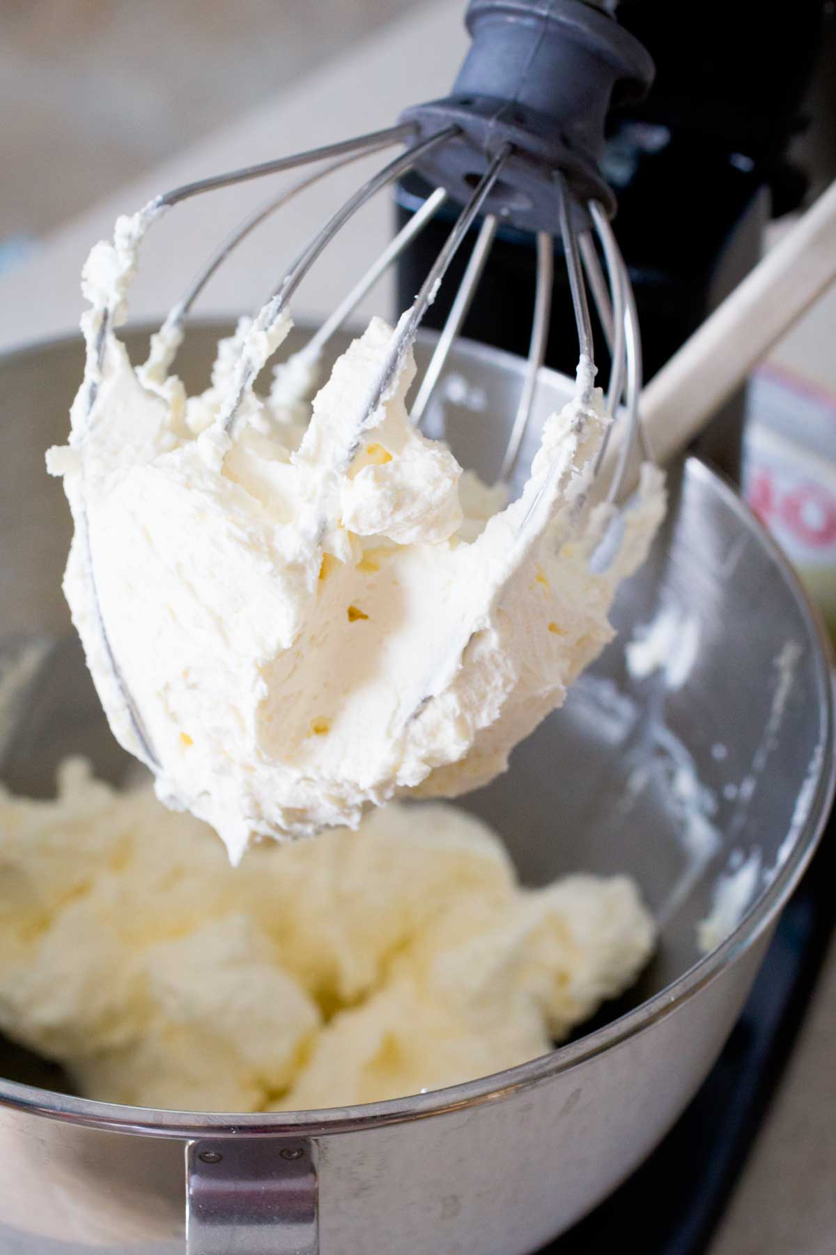 The whisk attachment on a stand mixer shows the texture of the thick, stabalized whipped cream.