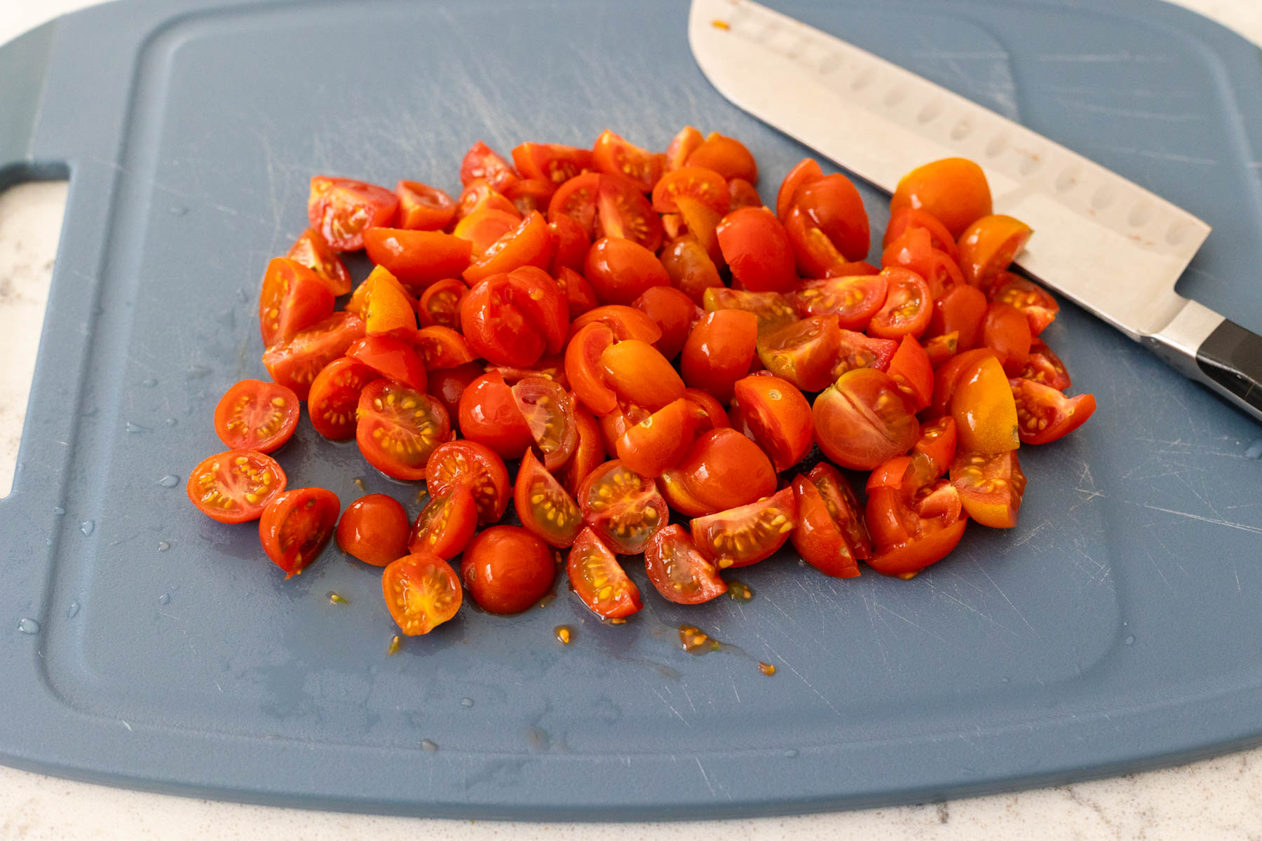 The cherry tomatoes have been chopped on a cutting board.