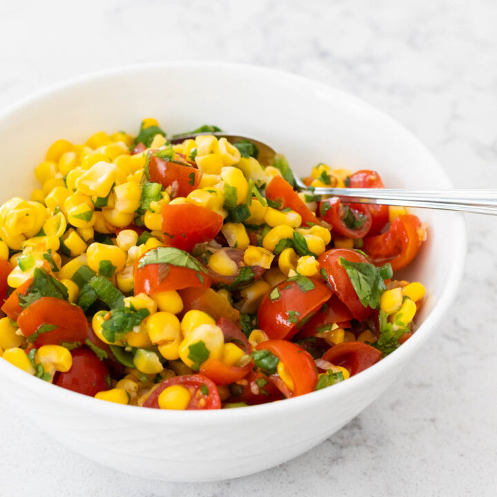 A white bowl filled with corn salsa has chopped cherry tomatoes stirred in.
