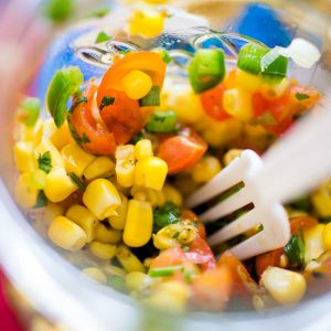 A jar of chunky corn salsa has fresh tomatoes, jalapeno peppers, and cilantro. There's a plastic fork digging in.