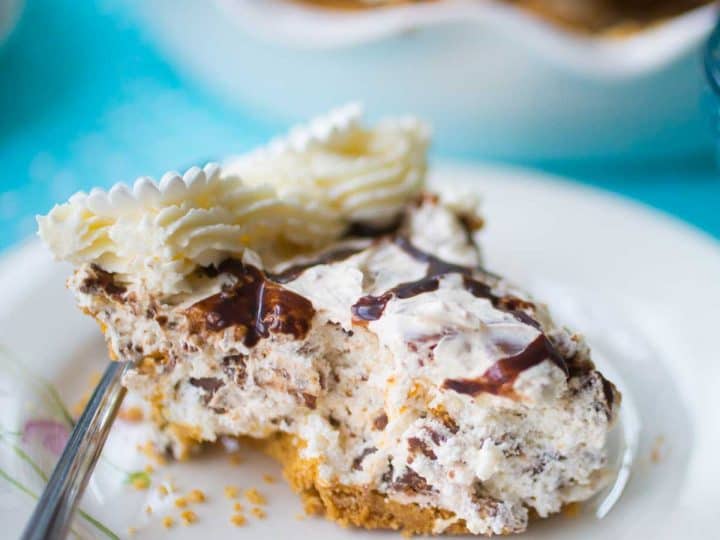 A slice of no bake butterfinger pie sits on a floral plate. You can see the graham cracker crust and whipped topping.