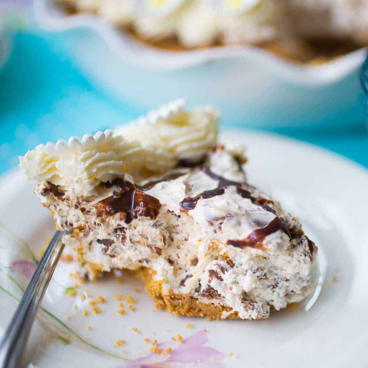 A slice of no bake butterfinger pie sits on a floral plate. You can see the graham cracker crust and whipped topping.