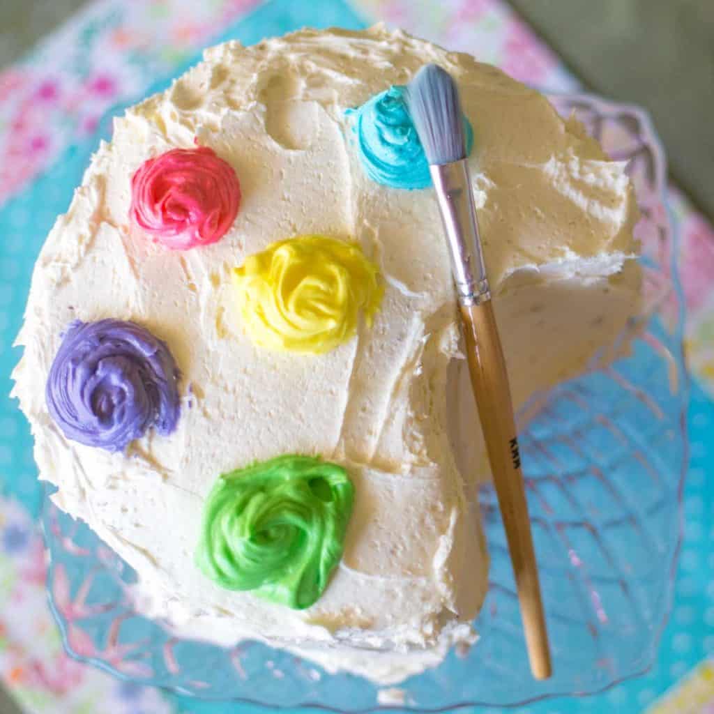 A birthday cake has been decorated to look like a paint palette with a paint brush on the side.