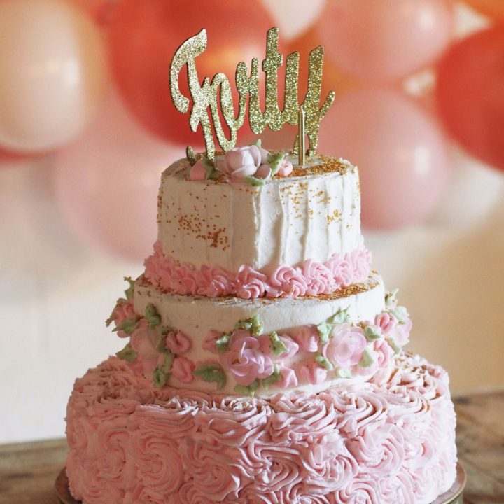 A pink and white birthday cake with a gold sparkly topper that says "Forty"