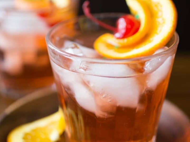 A glass of brandy old fashioned sweet has lots of ice and a maraschino cherry with orange twist for garnish.