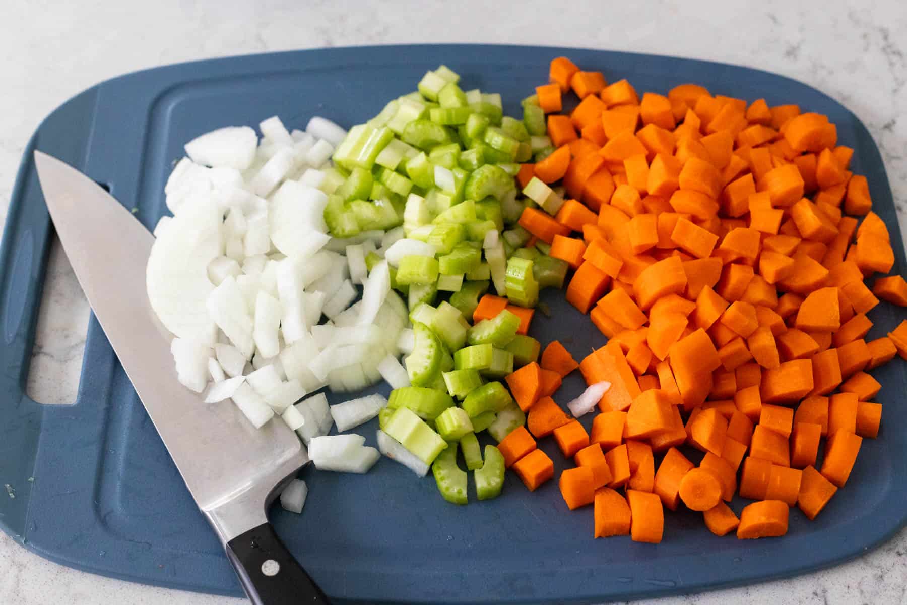 The onions, celery, and carrots have been diced on a cutting board.