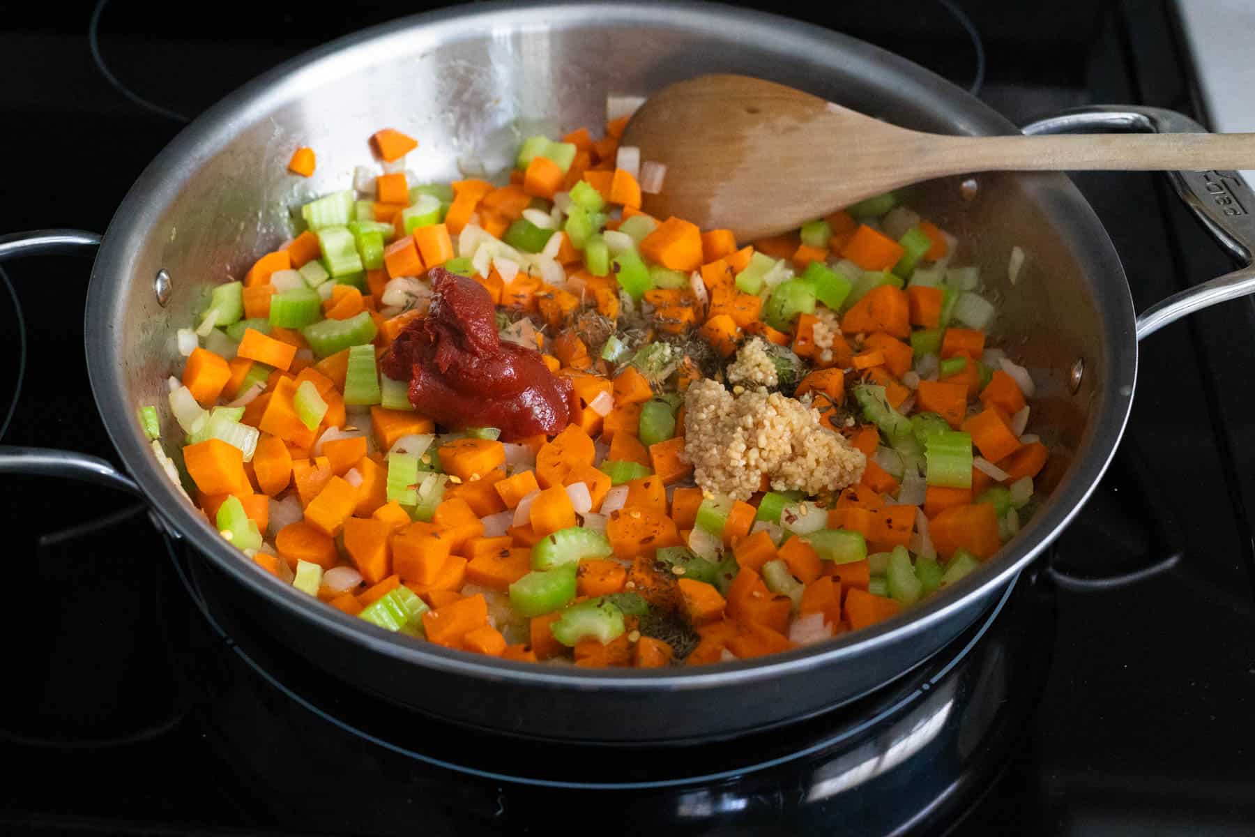 The tomato paste and minced garlic are on the vegetables in the skillet.
