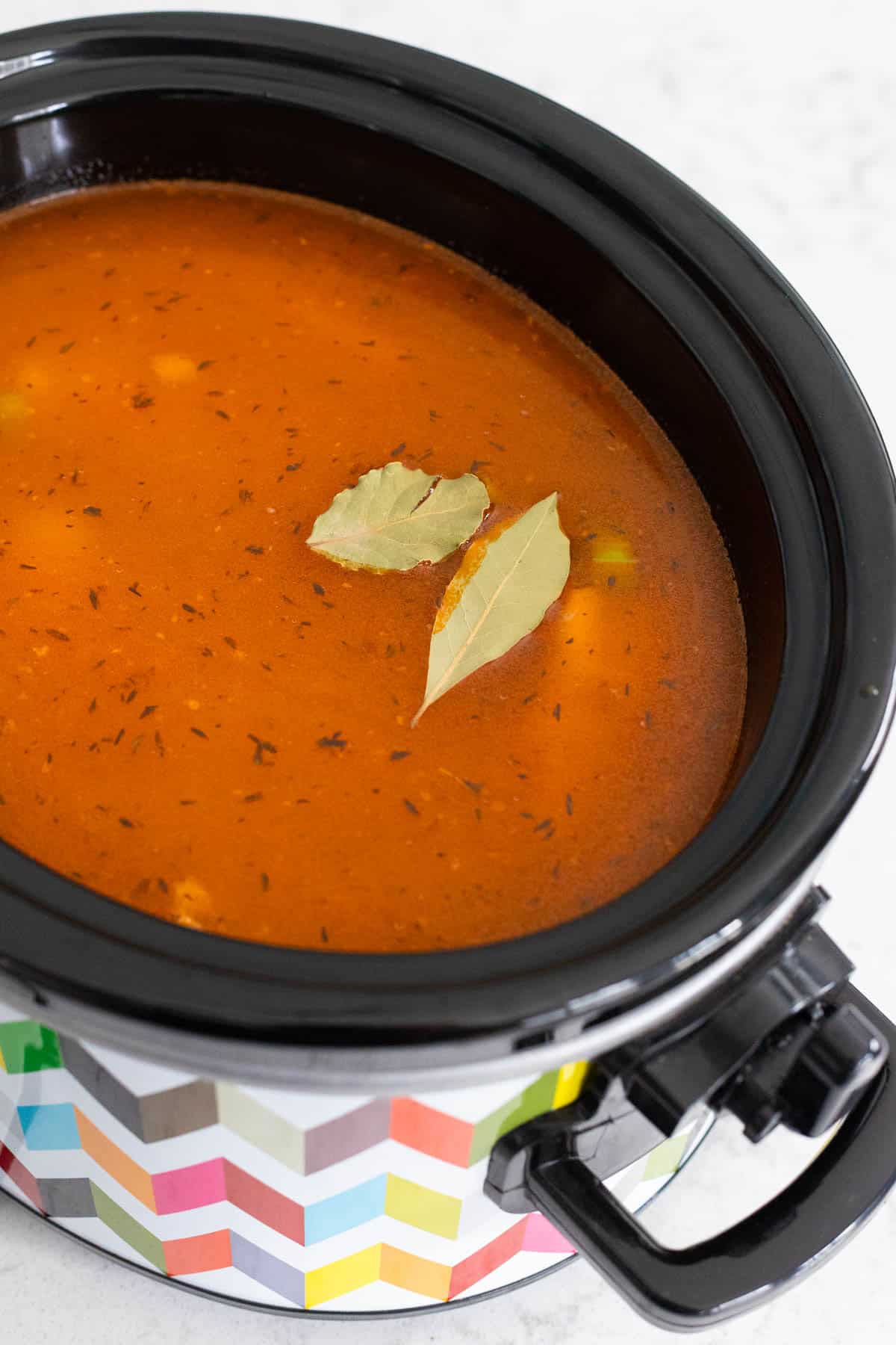 The remaining chicken stock, chicken, and bay leaves have been added to the crockpot.