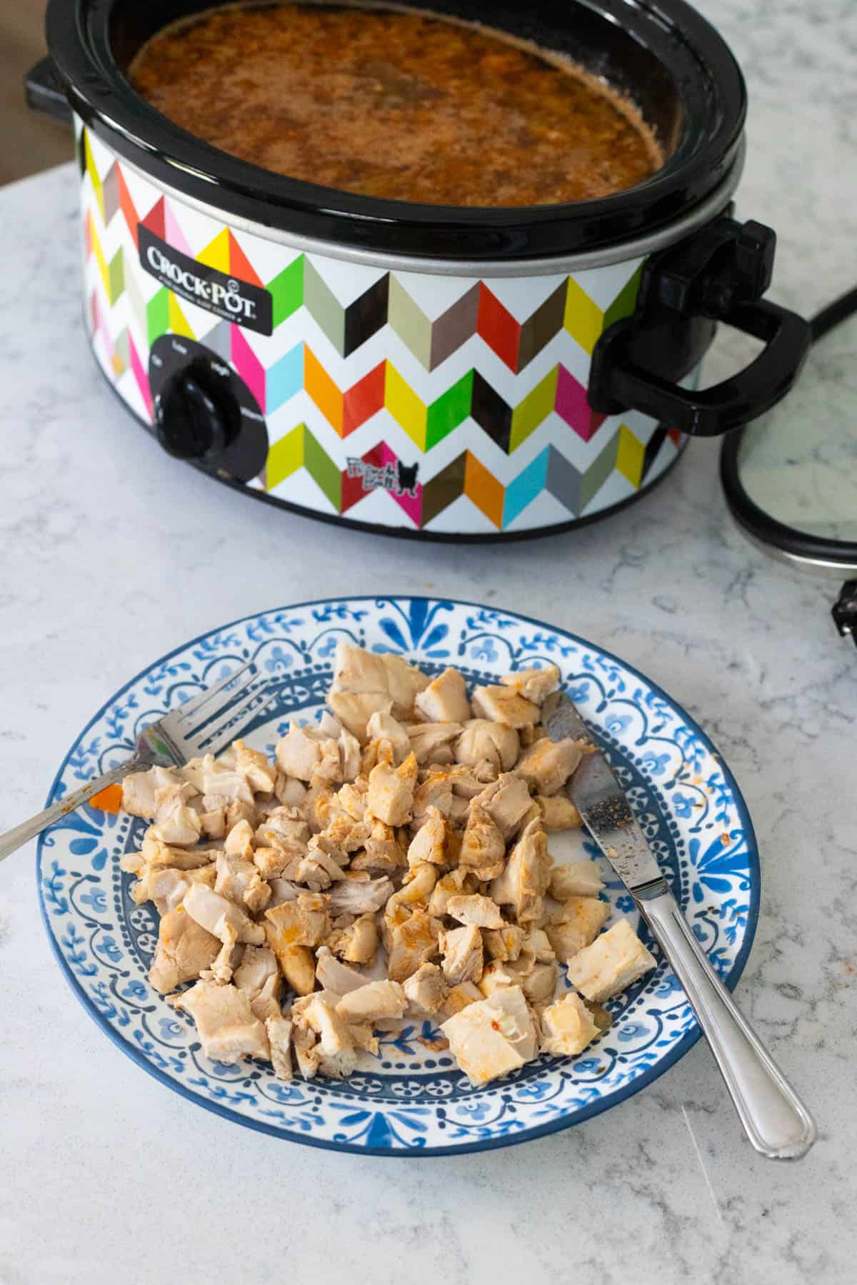The chicken thighs have been cut into diced chunks and are on a plate in front of the crockpot.