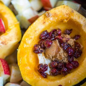 A sliced open acorn squash has been filled with red dried cranberries and a spoonful of brown sugar.